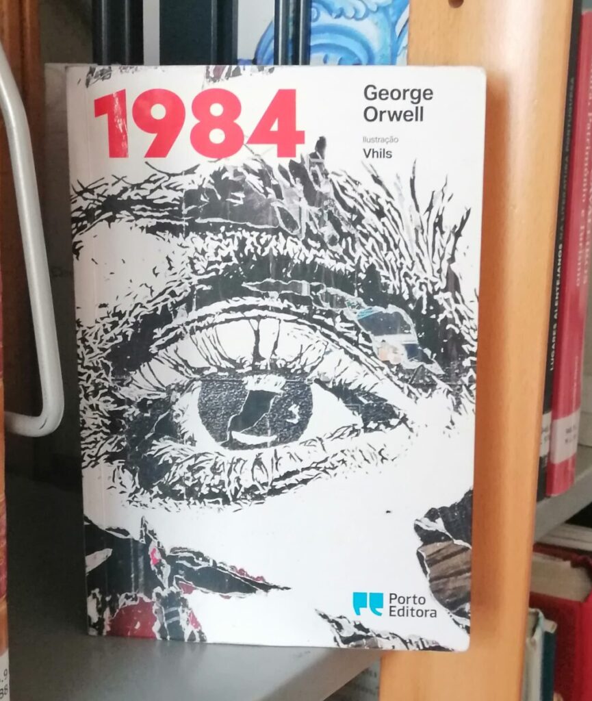 The cover of the Portuguese version of the book 1984 by George Orwell. The book is placed on a library shelf, facing the viewer, with a close up of a detailed realistic eye drawn in black ink, the title is bright red.